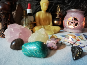 Halbedelsteine, Pendel und Tarotkarten vor Räucherstöchen mit Pentagramm, Buddha-Figuren und Tinktur-Fläschchen | Klopfecke